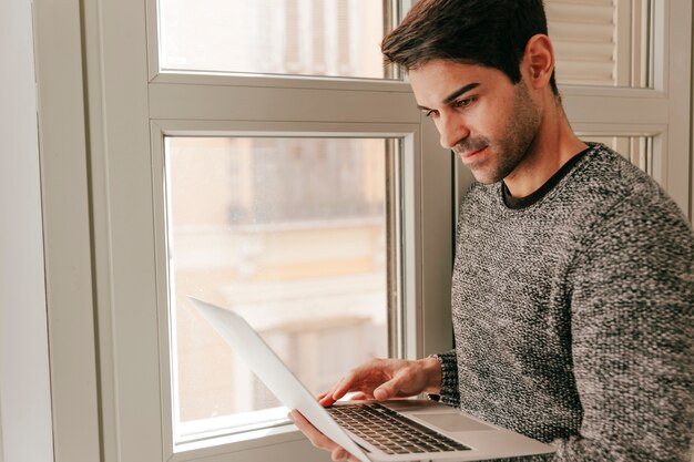 Foto gratuita uomo bello che utilizza computer portatile vicino alla finestra