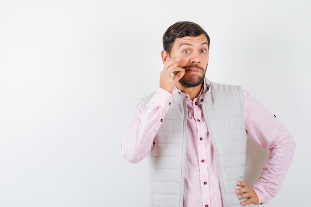 Free photo handsome man in vest, shirt showing zip gesture and looking anxious ,