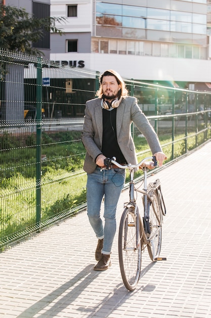 A handsome man walking with bicycle outside the building