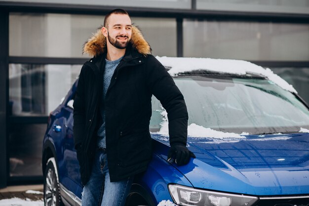 Handsome man in warm jacket standing by car covered with snow