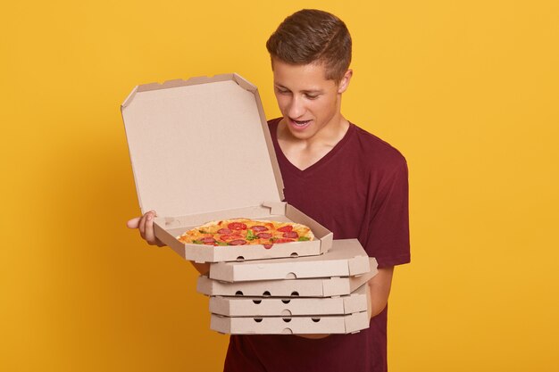 handsome man wearing burgundy casual t shirt, holding stack of pizza boxes in hands