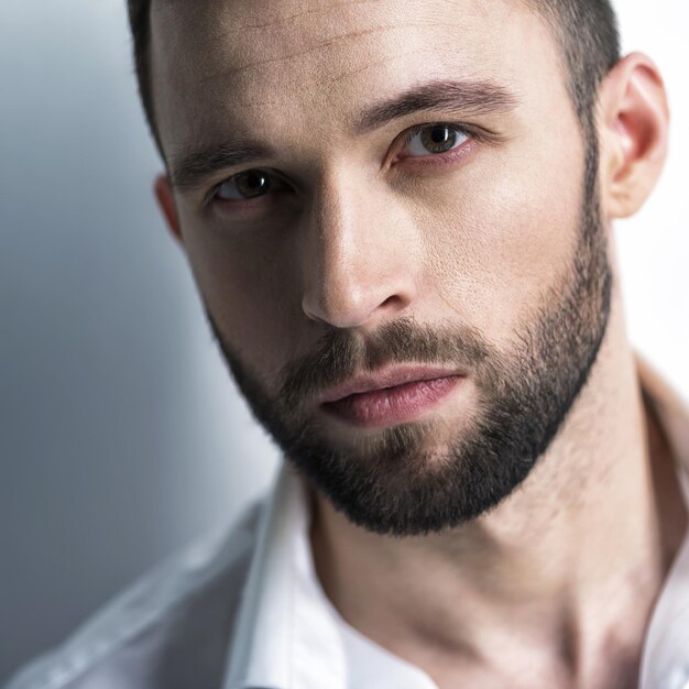 Handsome man in white shirt, posing   Attractive guy with fashion hairstyle.  Confident man with short beard. Adult boy with brown hair. Closeup portrait.