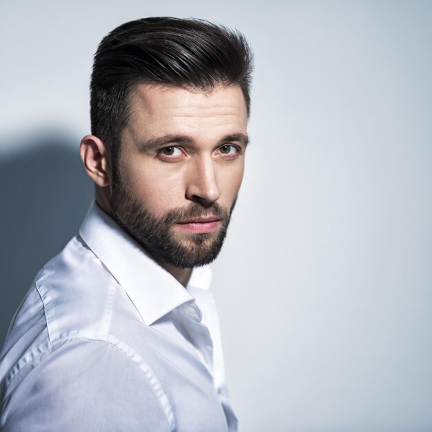 Handsome man in white shirt, posing   Attractive guy with fashion hairstyle.  Confident man with short beard. Adult boy with brown hair. Closeup portrait.
