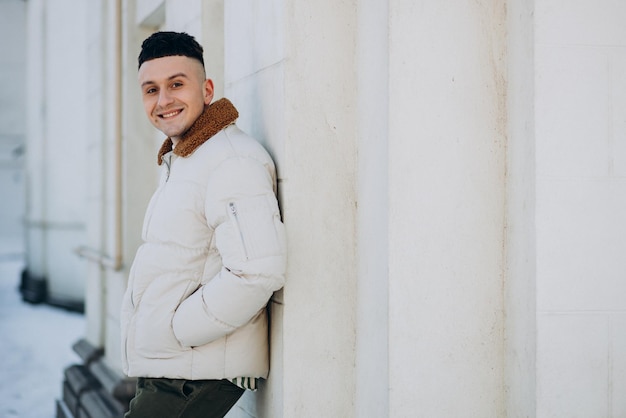 Handsome man in white winter jacket leaning on the wall