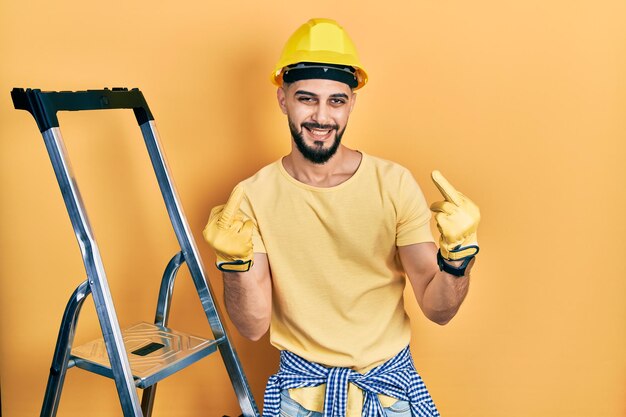 Free photo handsome man with beard by construction stairs wearing hardhat showing middle finger doing fuck you bad expression provocation and rude attitude screaming excited