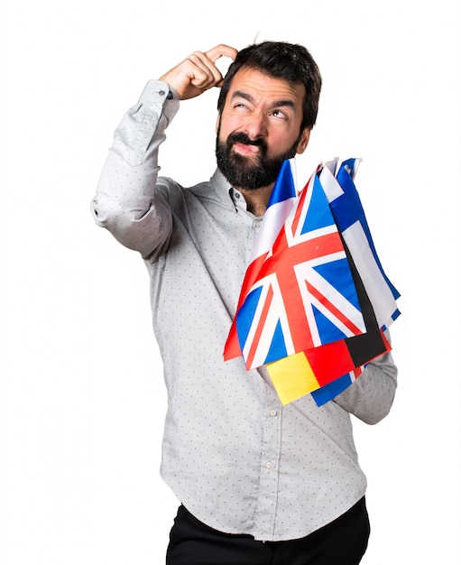 Free photo handsome man with beard holding many flags and having doubts