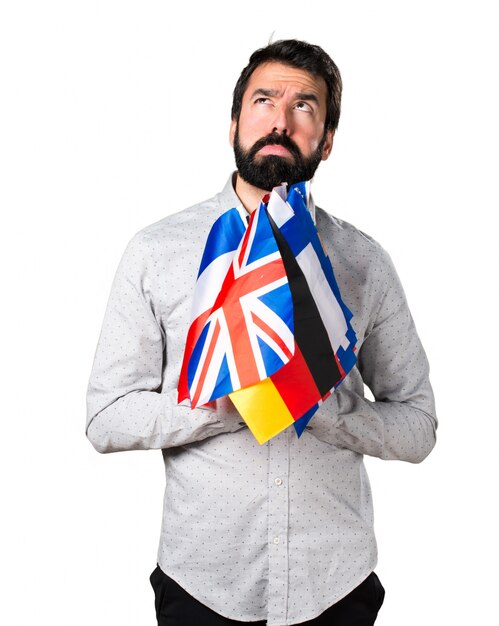 Handsome man with beard holding many flags and having doubts