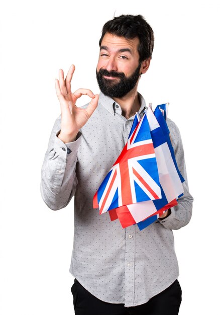 Handsome man with beard holding many flags and making OK sign