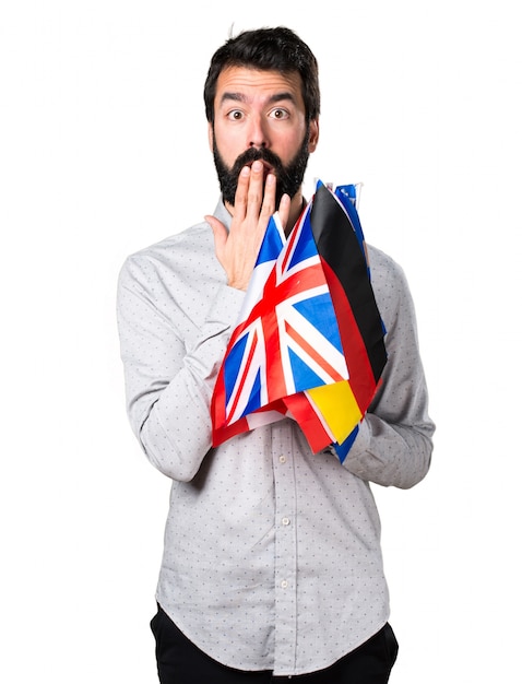 Handsome man with beard holding many flags and making surprise gesture