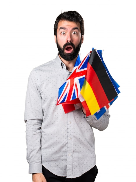 Handsome man with beard holding many flags and making surprise gesture