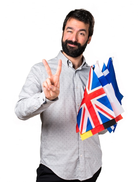 Handsome man with beard holding many flags and making victory gesture