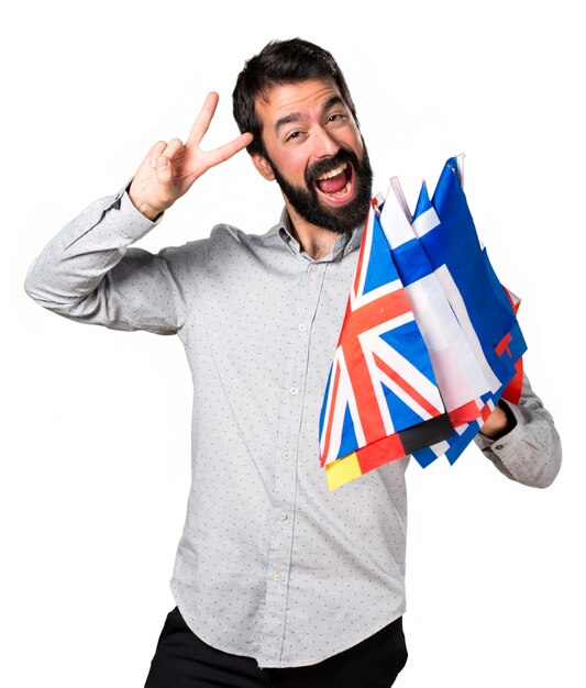 Handsome man with beard holding many flags and making victory gesture