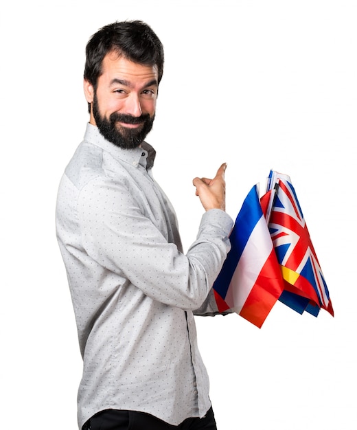 Foto gratuita uomo bello con la barba che tiene molte bandiere e che indica indietro