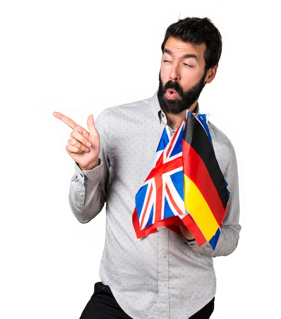 Handsome man with beard holding many flags and pointing to the lateral