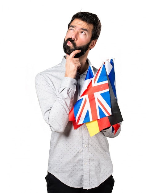 Free photo handsome man with beard holding many flags and thinking