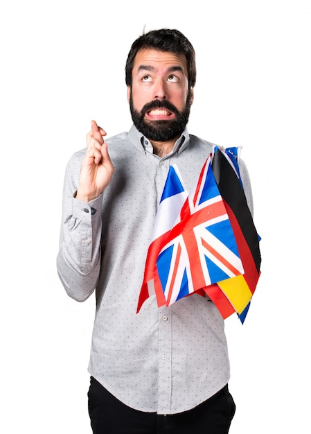 Free photo handsome man with beard holding many flags and with his fingers crossing