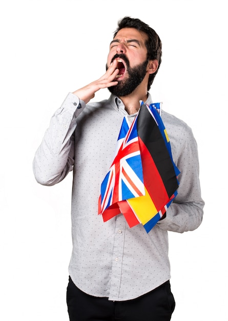 Free photo handsome man with beard holding many flags and yawning