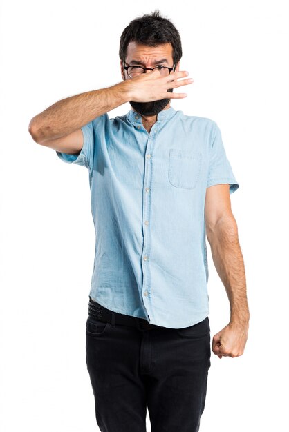 Handsome man with blue glasses making smelling bad gesture