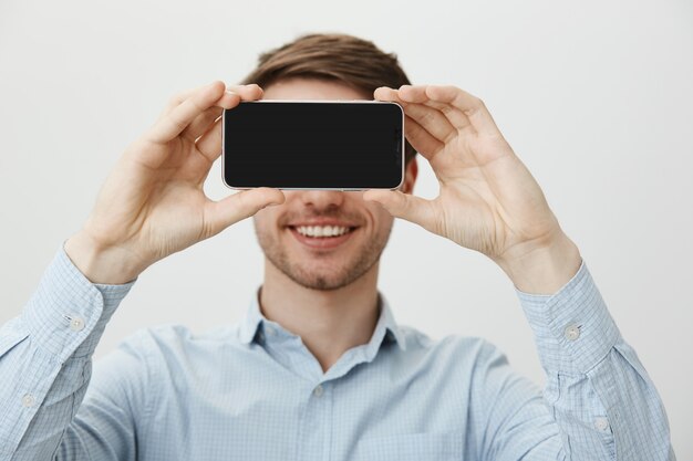 Handsome man with bristle, smiling showing smartphone display