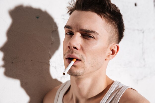 Красивый мужчина с сигаретой позирует на стене