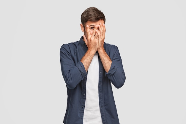 Free photo handsome man with dark hair, bristle, hides face with hands