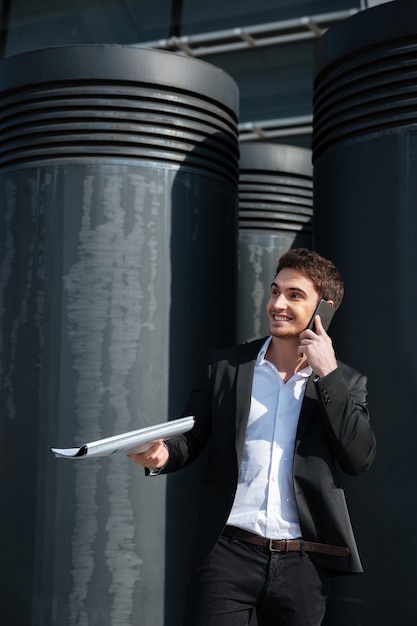 handsome man with documents talking on phone in the street