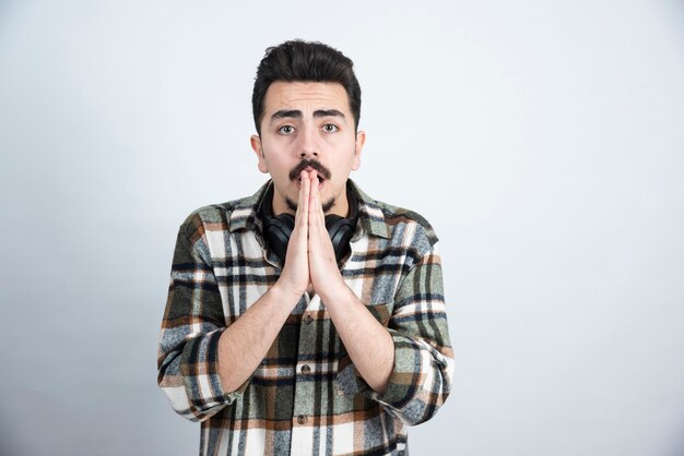 handsome man with headphones begging over white wall.