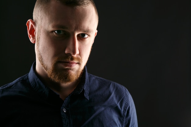 Handsome man with red beard poses on black background 