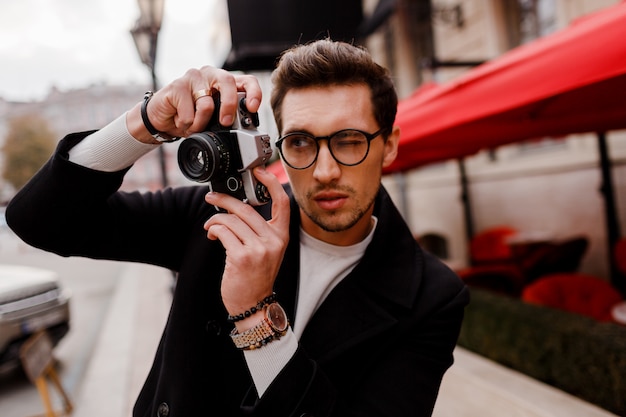 Handsome man with stylish hairstyle making photod in european city. Autumn season.