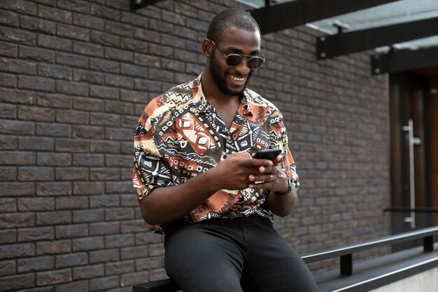 야외에서 현대적인 스마트폰을 사용하여 선글라스를 낀 잘생긴 남자