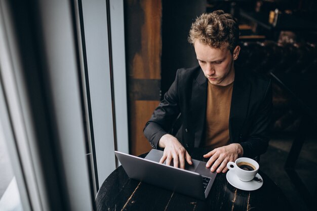 ハンサムな男がカフェでコンピューターに取り組んでいるとコーヒーを飲む