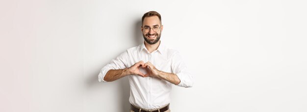 Handsome manage showing heart sign and smiling i love you gesture standing over white background