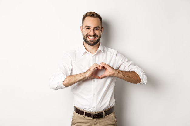 Handsome manage showing heart sign and smiling, I love you gesture, standing