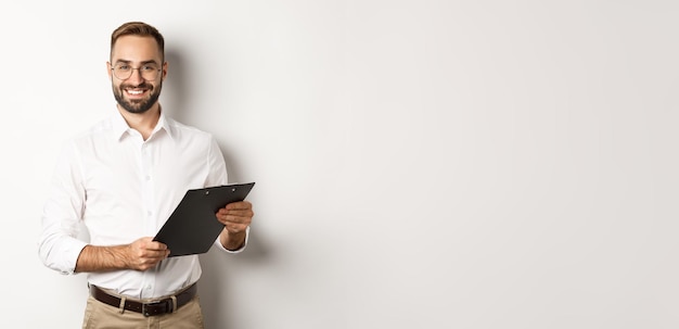 Handsome manager in glasses working using clipboard standing over white background