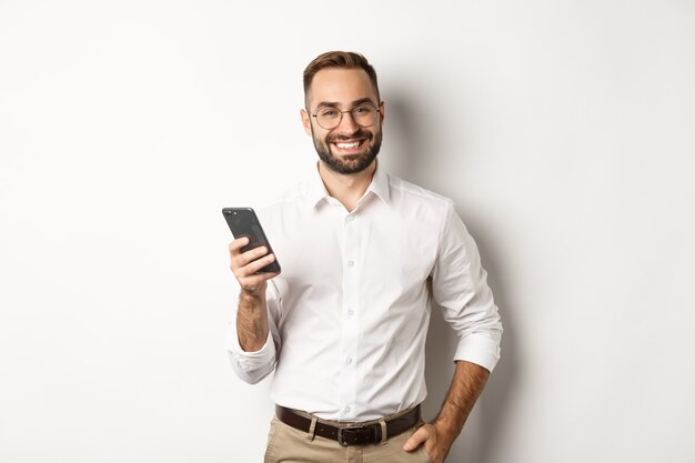 Handsome manager using smartphone and smiling pleased, sending text message, standing  .