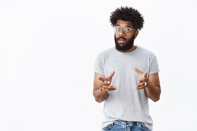 Handsome masculine bearded african american man in glasses with tattoos gesturing and waving hands as talking, explaining how product work raising eyebrows, describing thing to customer