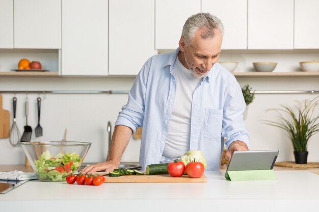 handsome mature man standing at the kitchen cooking salad.