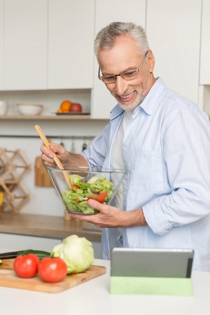 サラダを調理するキッチンに立っているハンサムな中年の男性。