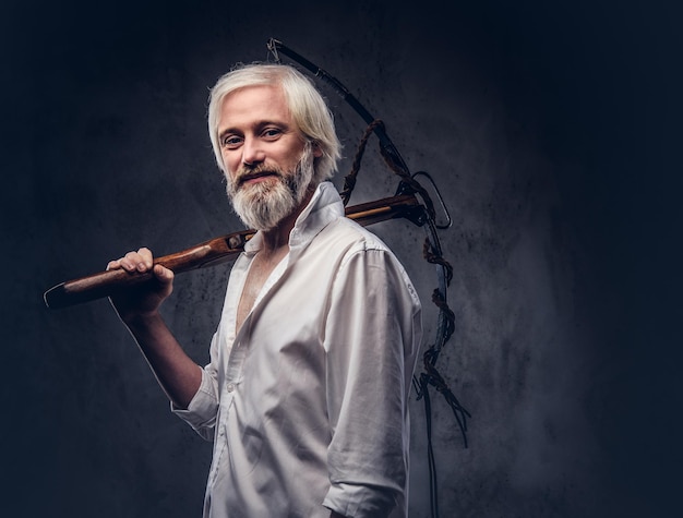 Free photo handsome mature man with a gray beard and white shirt holding a crossbow on shoulder