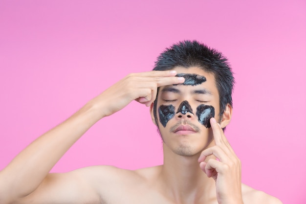 Handsome men are using their hands to apply black cream on their faces and have a pink .