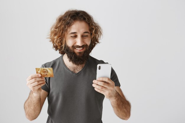 Foto gratuita bell'uomo mediorientale che compera online, tenendo la carta di credito e il cellulare