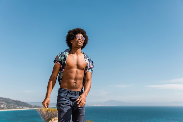 Красивый мускулистый афро-американский мужчина позирует на фоне голубого неба и моря