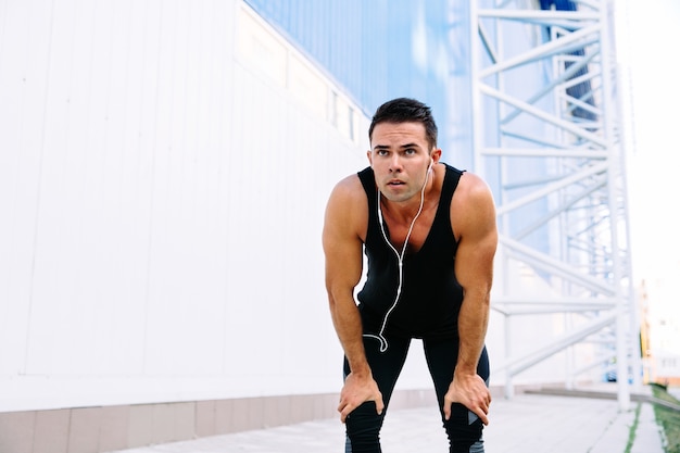 Handsome muscular man in headset resting after running, during workout outdoors