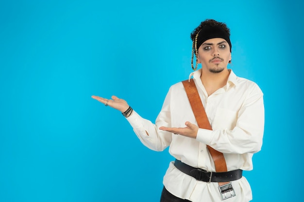 Handsome pirate stand on blue background and point hands to the right side. High quality photo