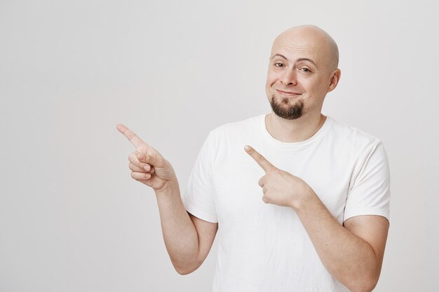 Free photo handsome pleased middle-aged man smiling and pointing left