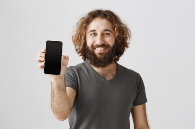 Handsome pleased middle-eastern man showing smartphone screen and smiling