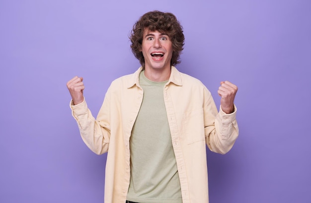 Free photo handsome positive happy young man isolated on purple background showing winner gesture