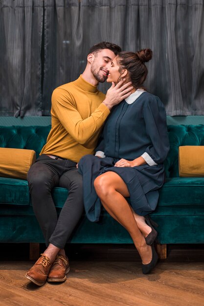 Handsome positive man kissing cheerful young woman on settee