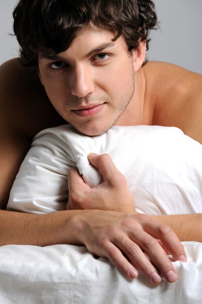 Handsome pretty young man lying in bed with pillow