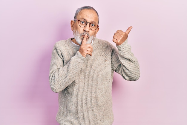 Free photo handsome senior man with beard wearing casual sweater and glasses asking to be quiet with finger on lips pointing with hand to the side. silence and secret concept.